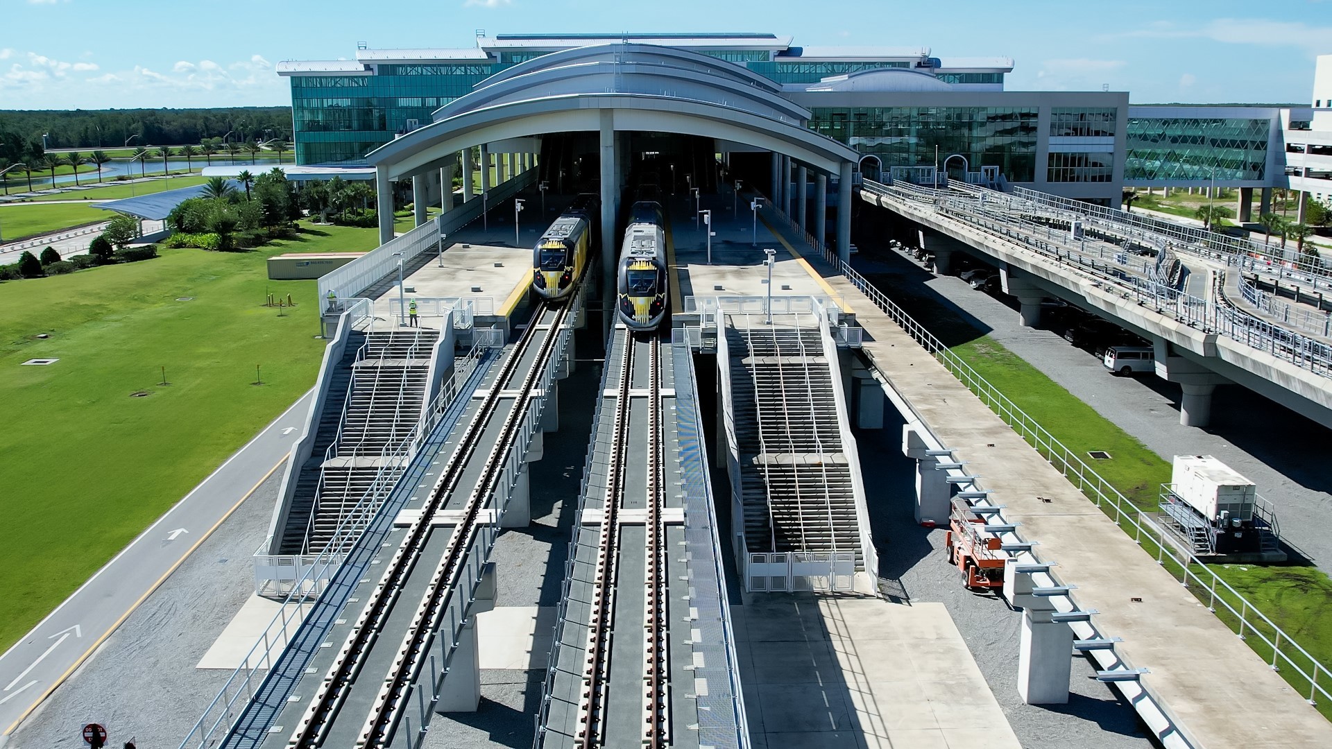 two brightline trains with yellow diagonal stripes next to MCO terminal C